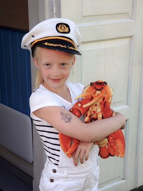 Helle med kapteinslue, tatovering og hummeren Harald på Kystmuseet.Foto Pål Bugge.